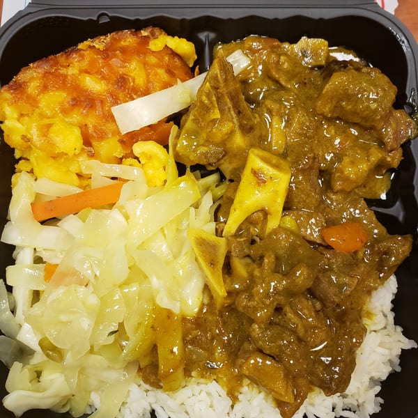 Jamaican Cafe Cuisine's curry goat with rice, mac and cheese, and steamed cabbage in a takeout container.
