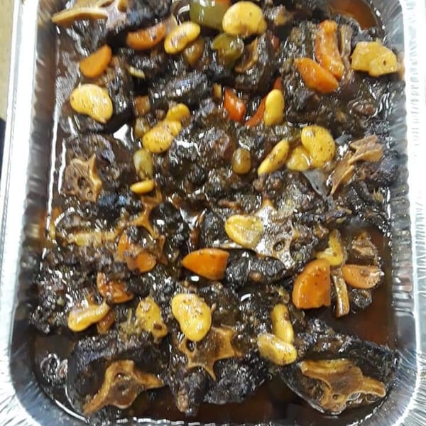 Close-up of Jamaican oxtail stew with butter beans and carrots in a foil pan.