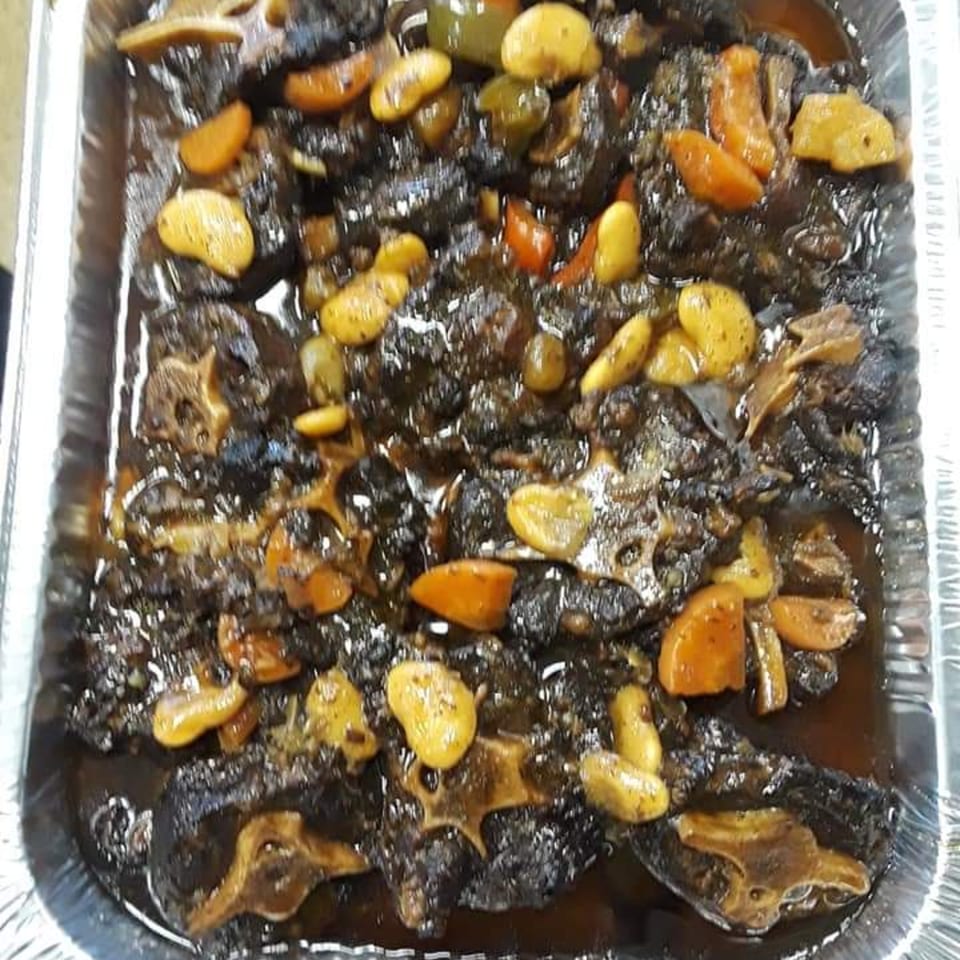Close-up of Jamaican oxtail stew with butter beans and carrots in a foil pan.