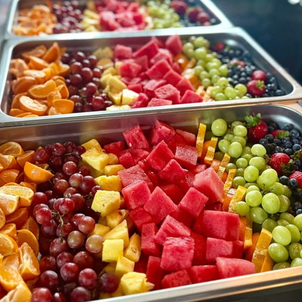Trays of colorful fresh fruit, including watermelon, grapes, oranges, pineapple, blueberries, and strawberries.