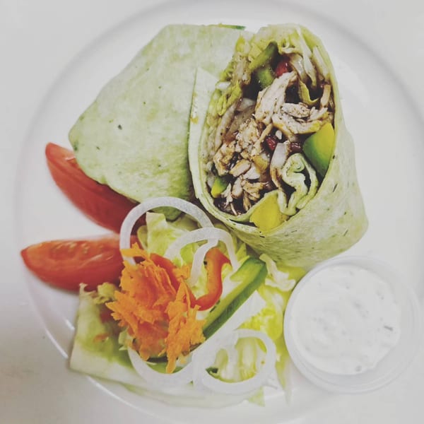 A Jamaican Cafe Cuisine chicken wrap, cut in half, with a side salad and dipping sauce.
