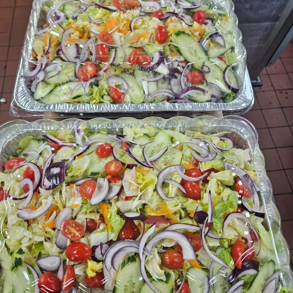 Two foil trays of fresh garden salad with lettuce, tomatoes, cucumbers, and red onions.