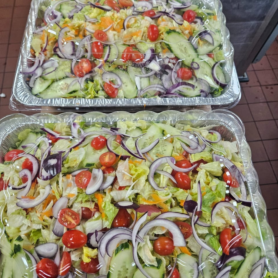 Two foil trays of fresh garden salad with lettuce, tomatoes, cucumbers, and red onions.